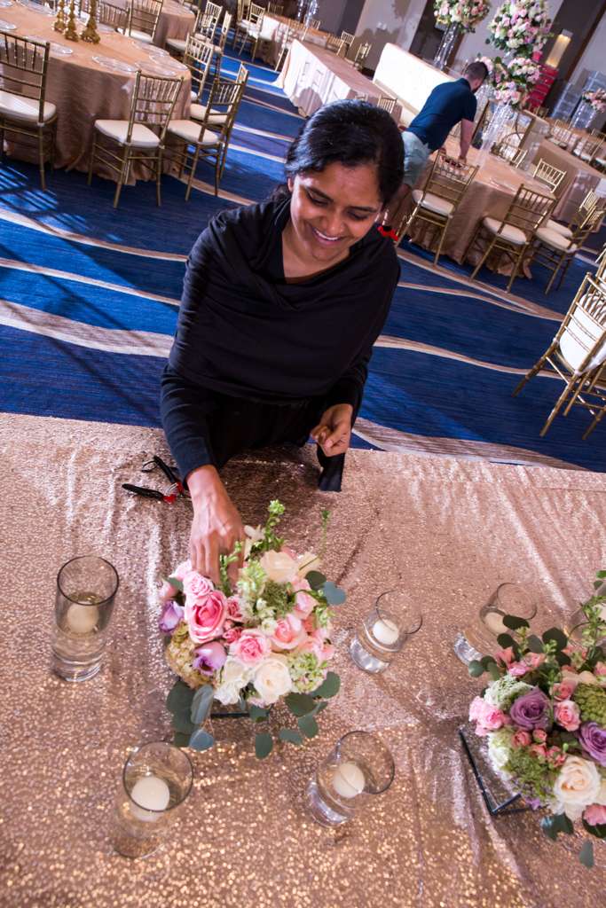 Jilna arranging a centerpiece of pink and white roses on a sequined table at a Suhaag Garden wedding