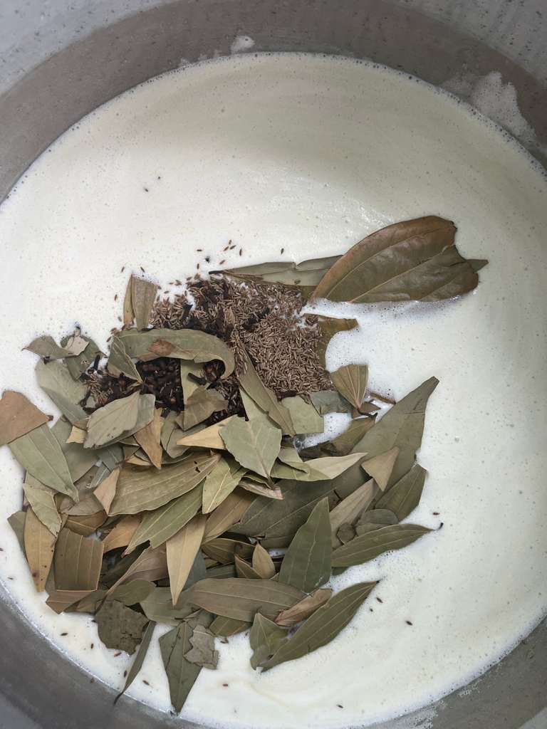 Whole spices during preparation: bay leaves, cumin seeds and cloves added to a steel pot